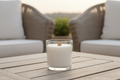 create a white votive candle with a wood wick in a clear glass votive holder with a patio table background 